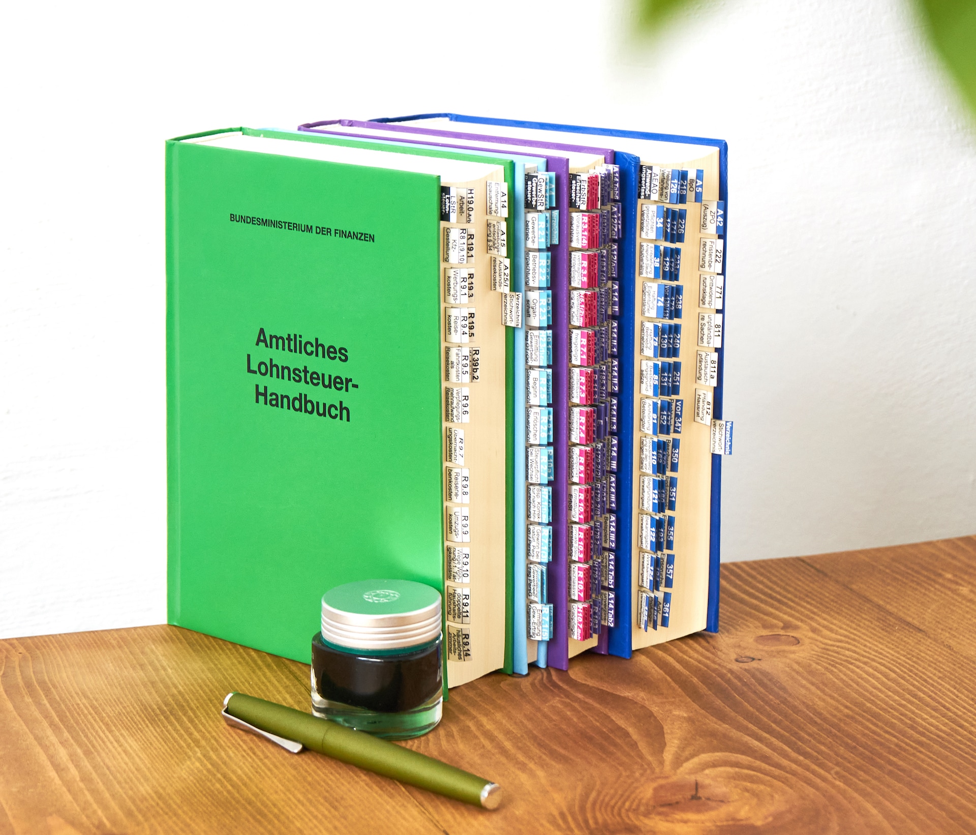 BMF Handbücher stehen nebeneinander mit eingeklebten Griffegistern auf einem Schreibtisch.